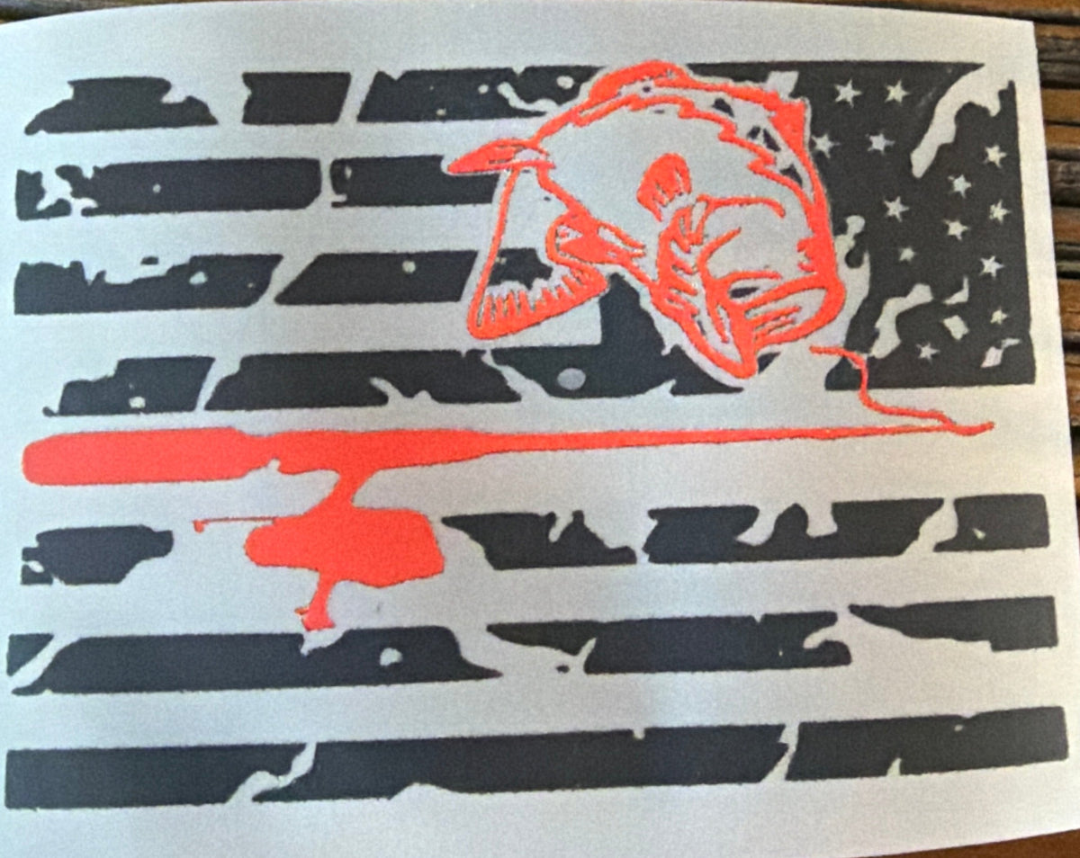 A rectangular decal sticker featuring a distressed black American flag design with a red bass & fishing pole, placed on a dark brown wooden surface.