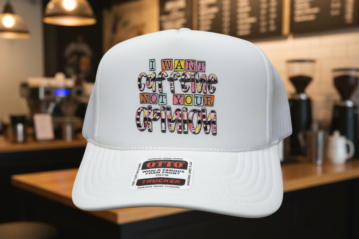 A white trucker hat with a foam front panel and mesh side/back panels. The front has a large rectangular graphic with the phrase “I WANT COFFEE NOT YOUR OPINION” in multicolored block letters.