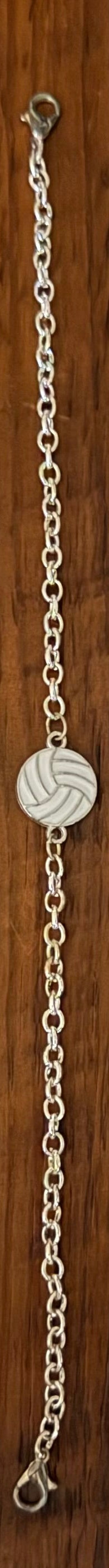 Four beaded and chain bracelets laid flat on a dark wood background. Three bracelets feature black and white beads with silver-toned links, and one bracelet features a yellow and blue volleyball charm on a silver chain.