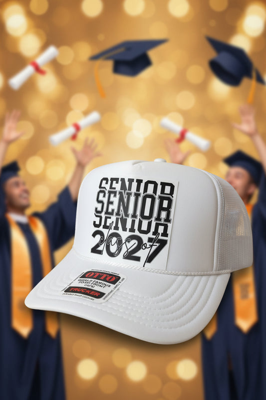 A white trucker-style cap with a white front patch reading 'SENIOR SENIOR class of 2027' in black text, photographed on a dark wood surface.