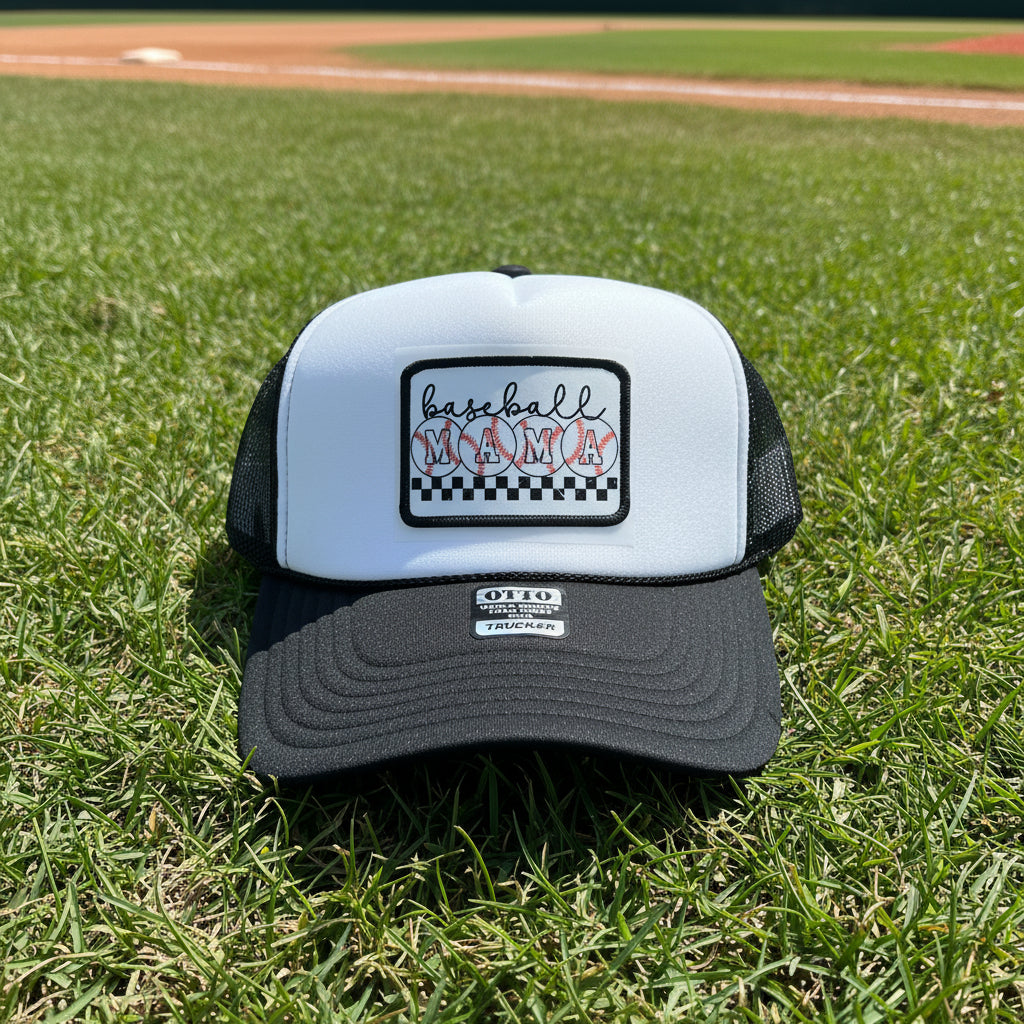 A black and white trucker hat with a white front panel and black mesh sides. The front features a rectangular patch with the text 'baseball MAMA' in black script and red baseball stitching over red-and-white striped circles, set against a black-and-white checkered border.