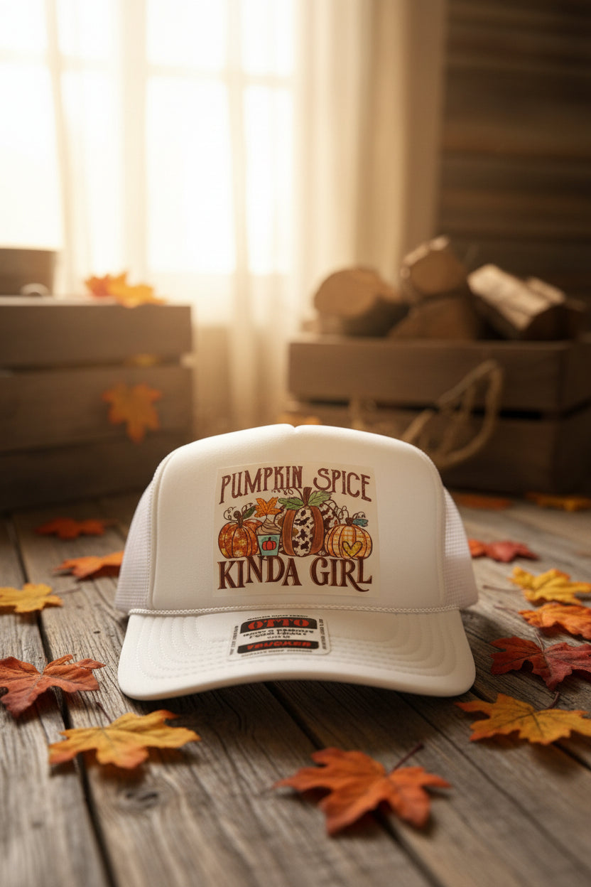 A white trucker cap with a 'Pumpkin Spice Kinda Girl' graphic on the front, resting on a dark wooden surface.