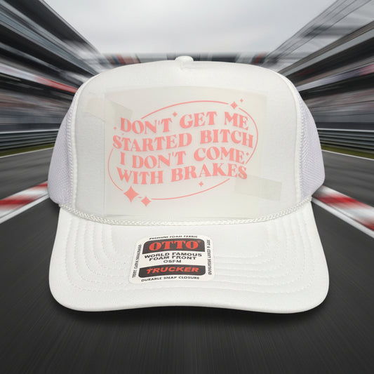 A white trucker hat with a pink graphic on the front that reads 'DON'T GET ME STARTED BITCH I DON'T COME WITH BRAKES' and a visible Otto brand sticker on the brim, set against a dark wood background.