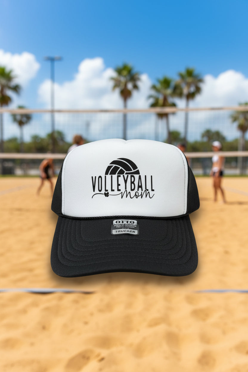A black and white trucker hat with 'VOLLEYBALL mom' printed on the front.