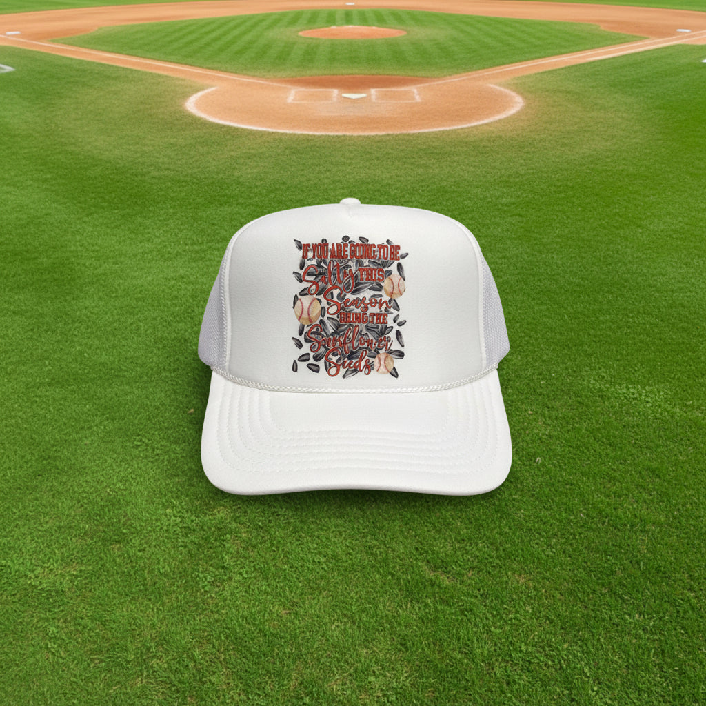 A white trucker hat with a custom graphic on the front panel that reads 'If You Are Going To Be salty this season bring The Sunflower Seeds' surrounded by sunflower illustrations. The brim features a visible 'OTTO' sticker, and the hat is photographed against a dark wood background.