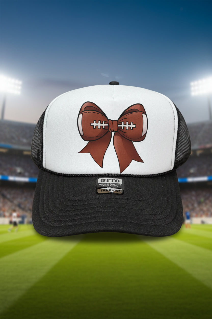 A black and white trucker hat with a brown and white football bow graphic on the front panel.