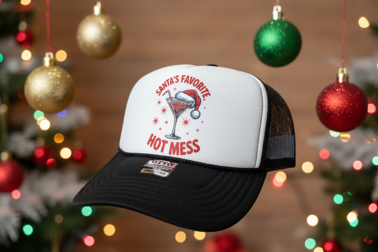 A black and white trucker hat with a red and white graphic on the front that reads 'SANTA'S FAVORITE, HOT MESS' around an illustration of a martini glass with a Santa hat. 
