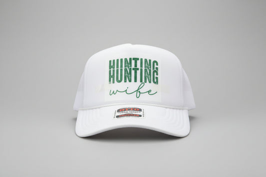 A white trucker hat with a white foam front panel and mesh back, featuring the words 'HUNTING wife' in green on the front. The brim has a visible 'OTC' sticker.